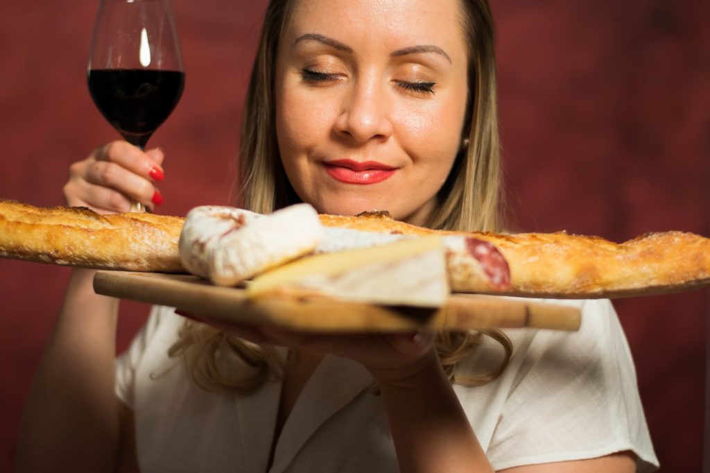 Jasmina presents her wine and cheese tasting in Paris while holding cheese and baguette